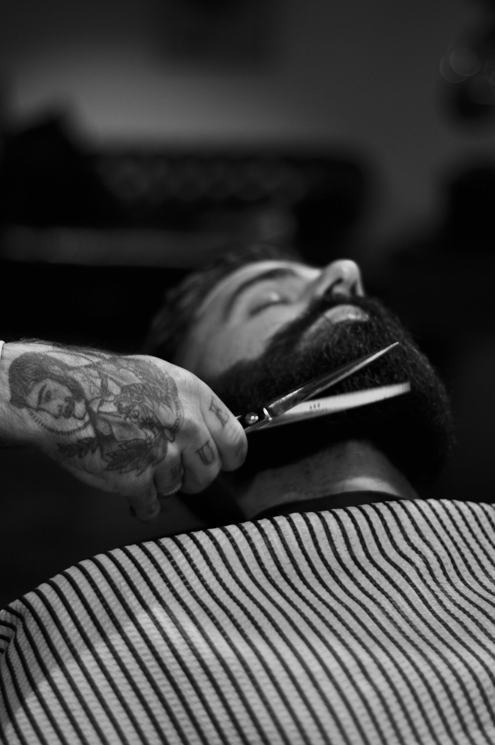 Fadehouse barber shaping a reclined client's beard with shears