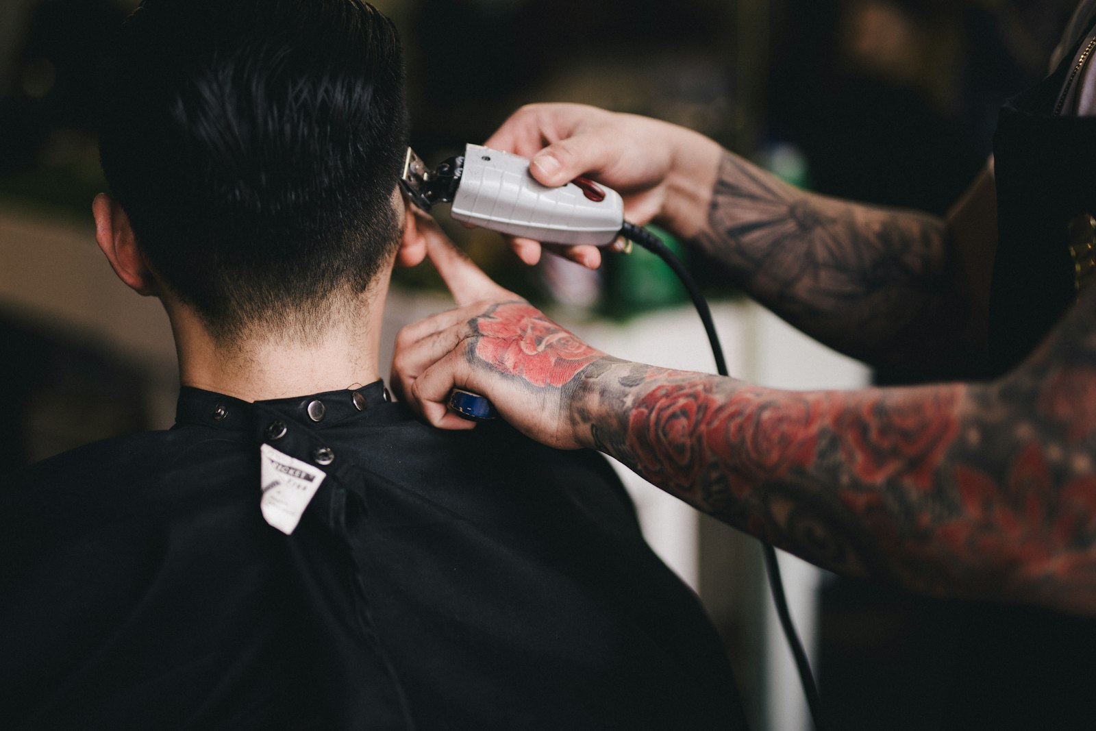 Tattooed barber running clippers up the nape of a client's neck