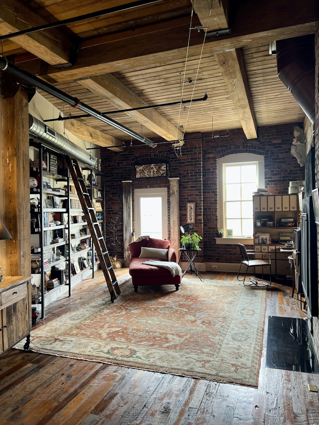 The Foxglove Books shop floor: exposed brick, timber beams, a rolling ladder against a full-height bookcase and a red velvet chaise.