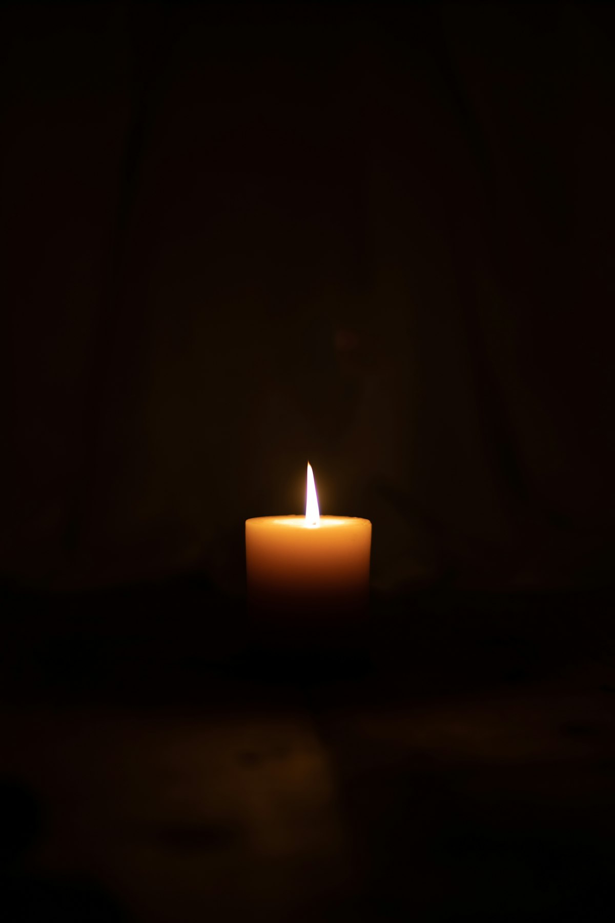 A single lit candle burning in a darkened room, its flame the only source of light.