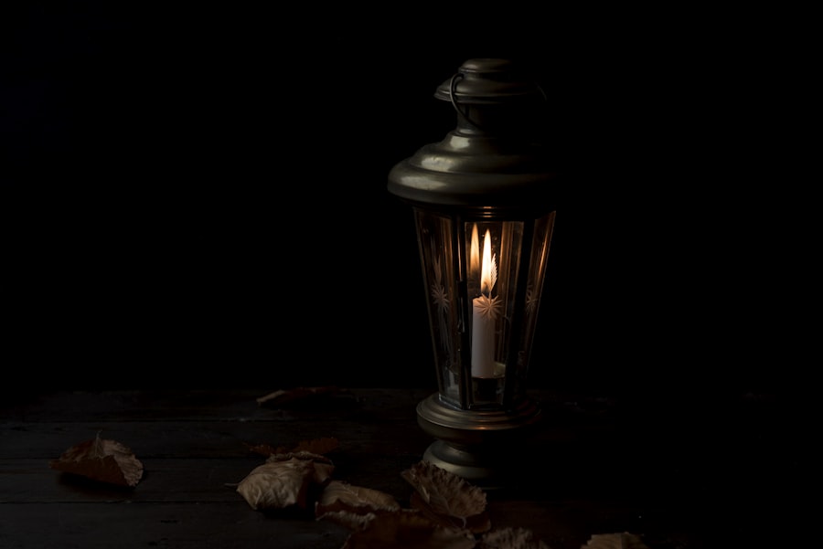 A candle burning inside an antique glass-panelled lantern on a dark wooden table scattered with dried leaves.