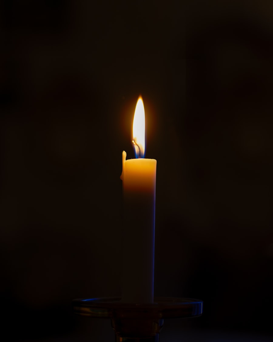 A single tall taper candle burning with a steady flame against a pitch-black background.