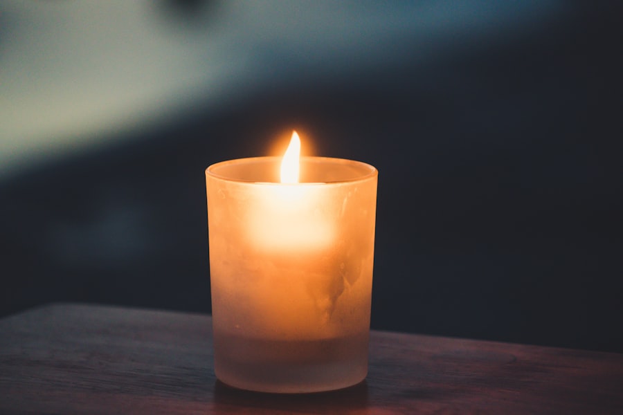A candle burning in a frosted glass votive on a wooden table, its flame the warmest point in a cool dark room.