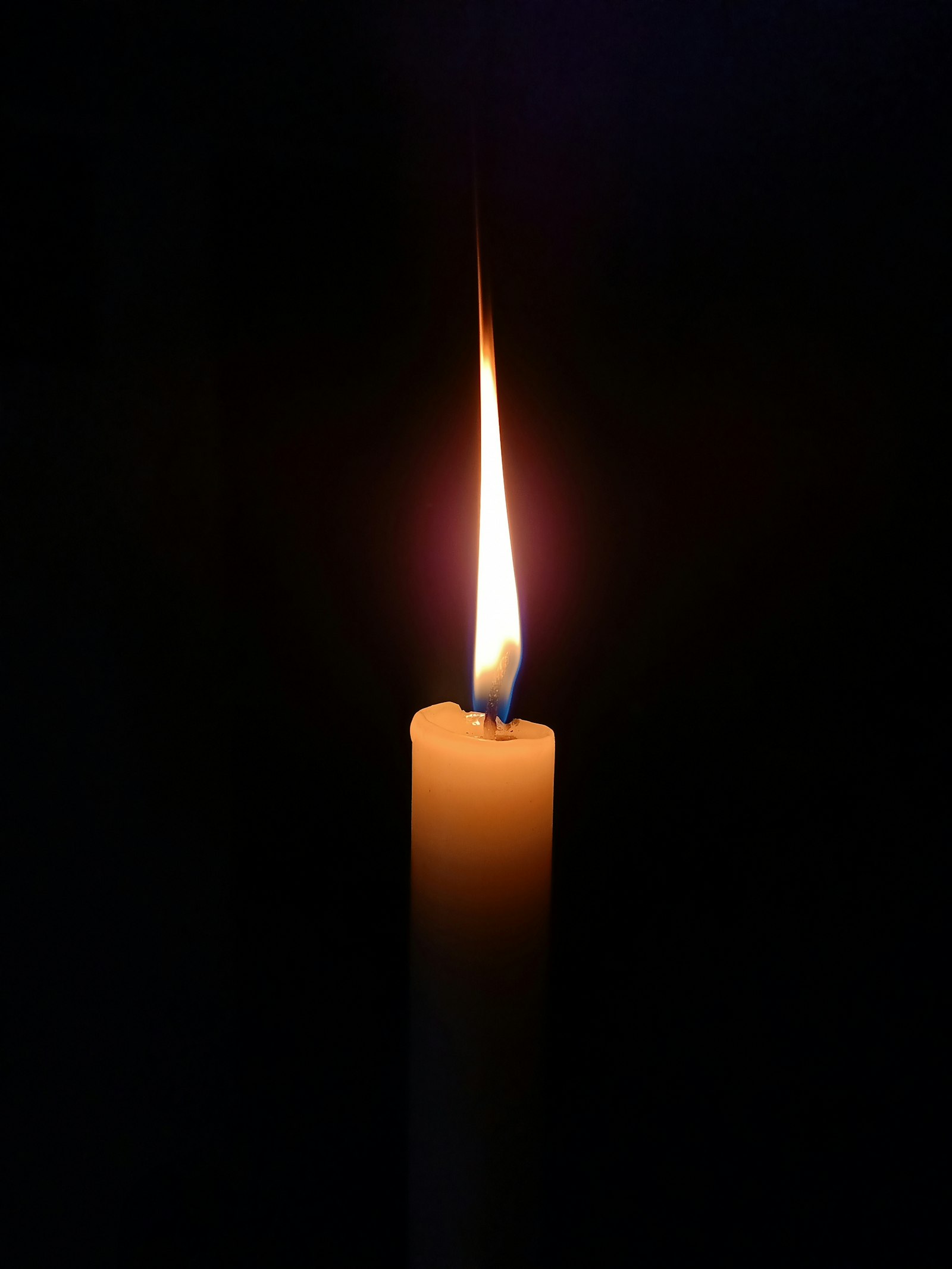 A single tall taper candle burning with a steady flame against a black background.