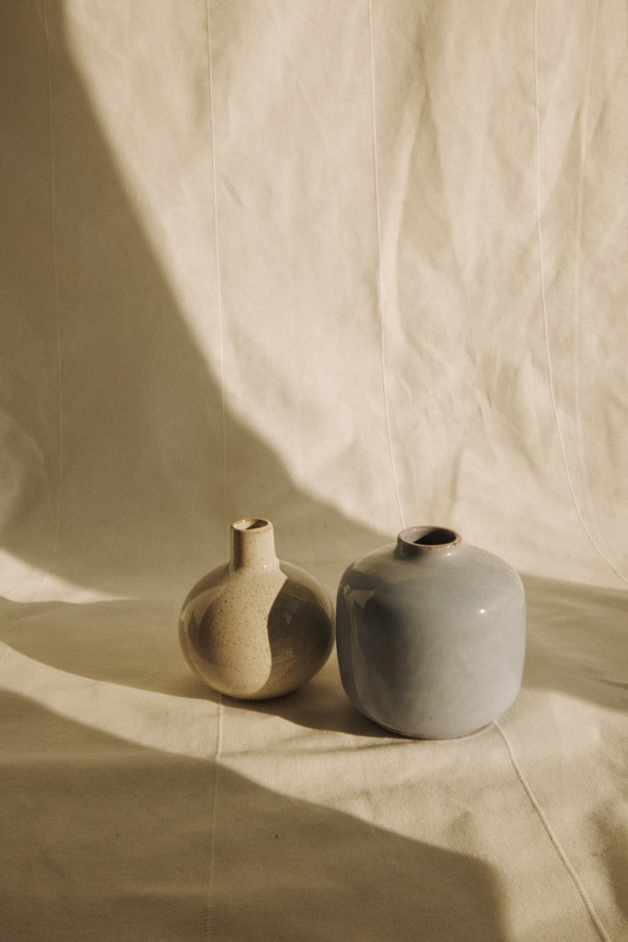 A speckled bottle vase next to a pale-blue glazed bud vase on folded linen.