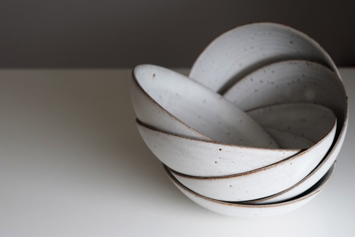 Four speckled white stoneware bowls stacked at an angle on a pale surface.