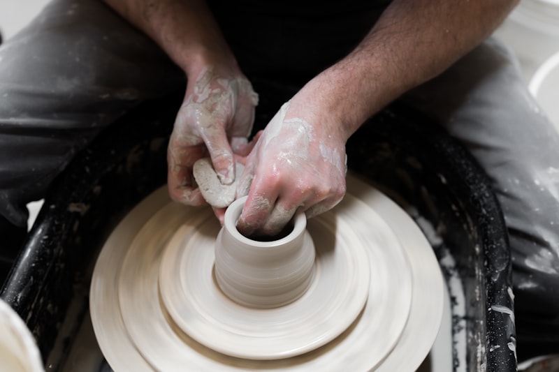 A potter's hands pulling up the wall of a cylinder on a spinning wheel head.