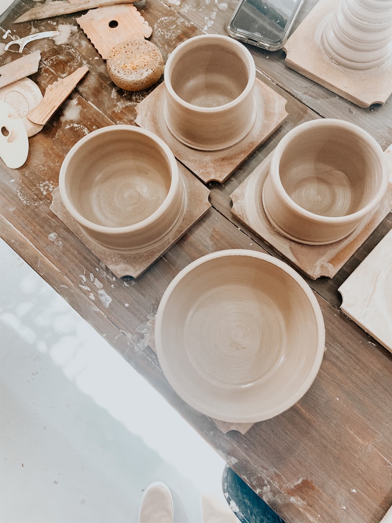 Freshly thrown greenware bowls and cups drying on wooden bats on a studio workbench beside trimming tools.