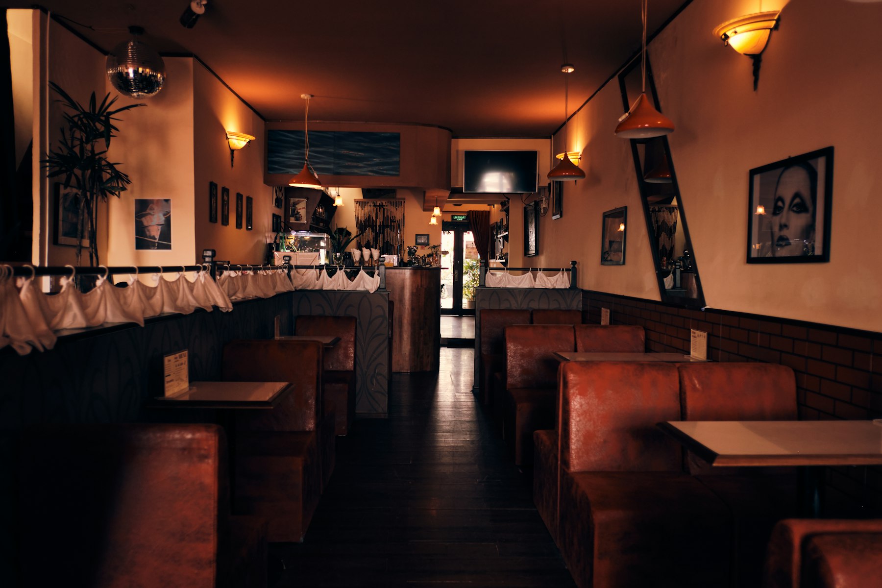 A warmly lit bar room lined with worn leather booth seating, small tables and low pendant lamps.