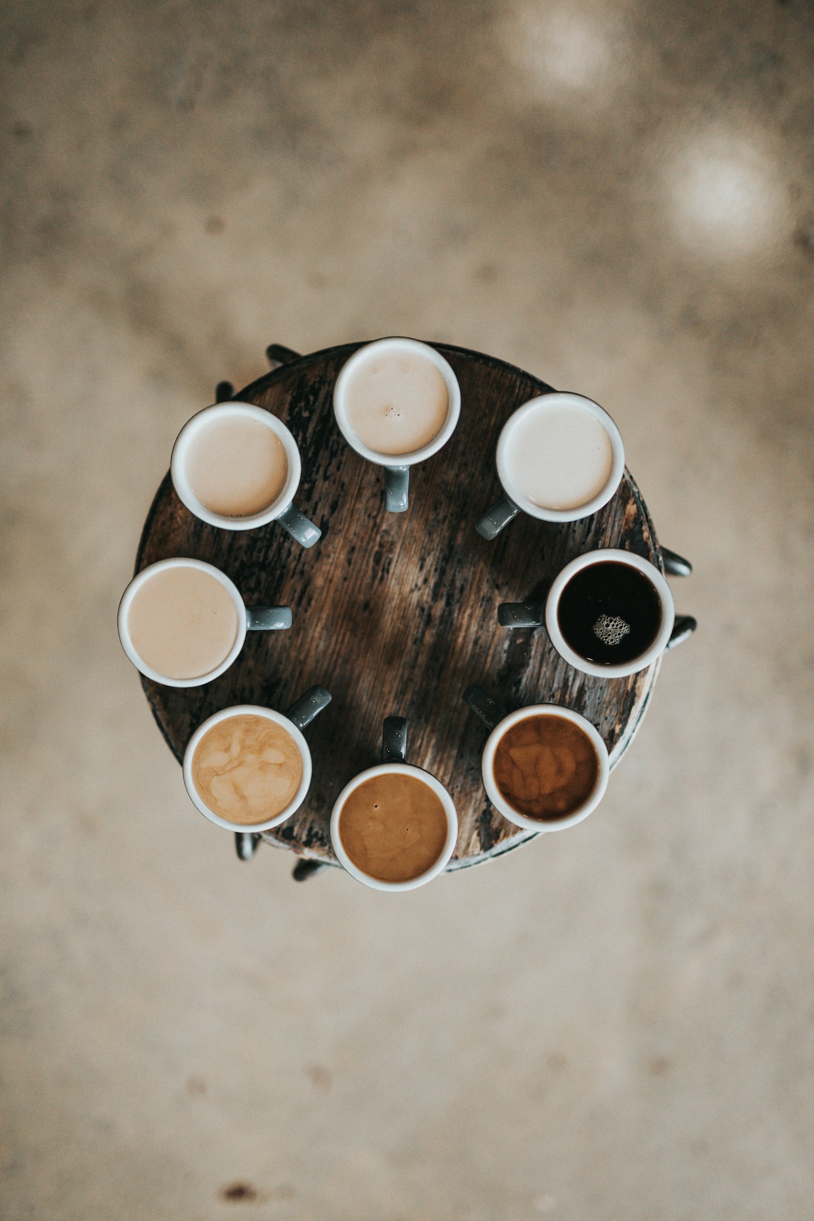 Eight cups of coffee arranged in a circle on a wooden table for a cupping
