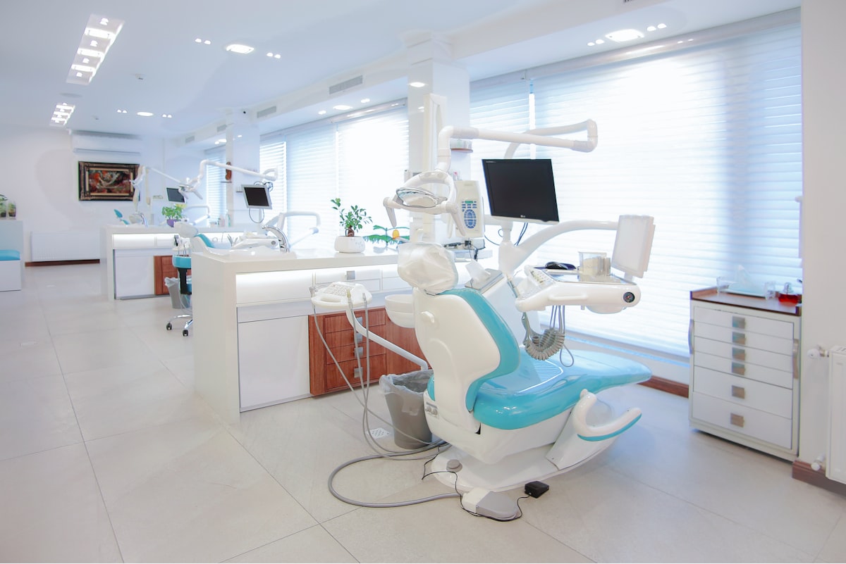 Open treatment bay with two teal dental chairs and daylight through wide blinds