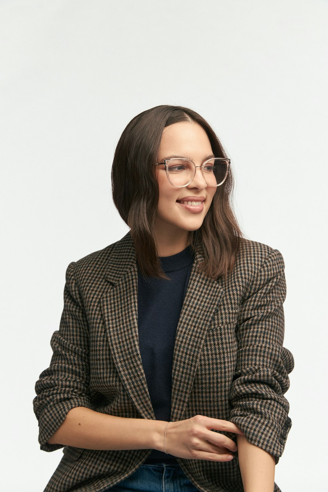 A woman in a checked blazer wearing clear cat-eye Lunet frames, looking off camera