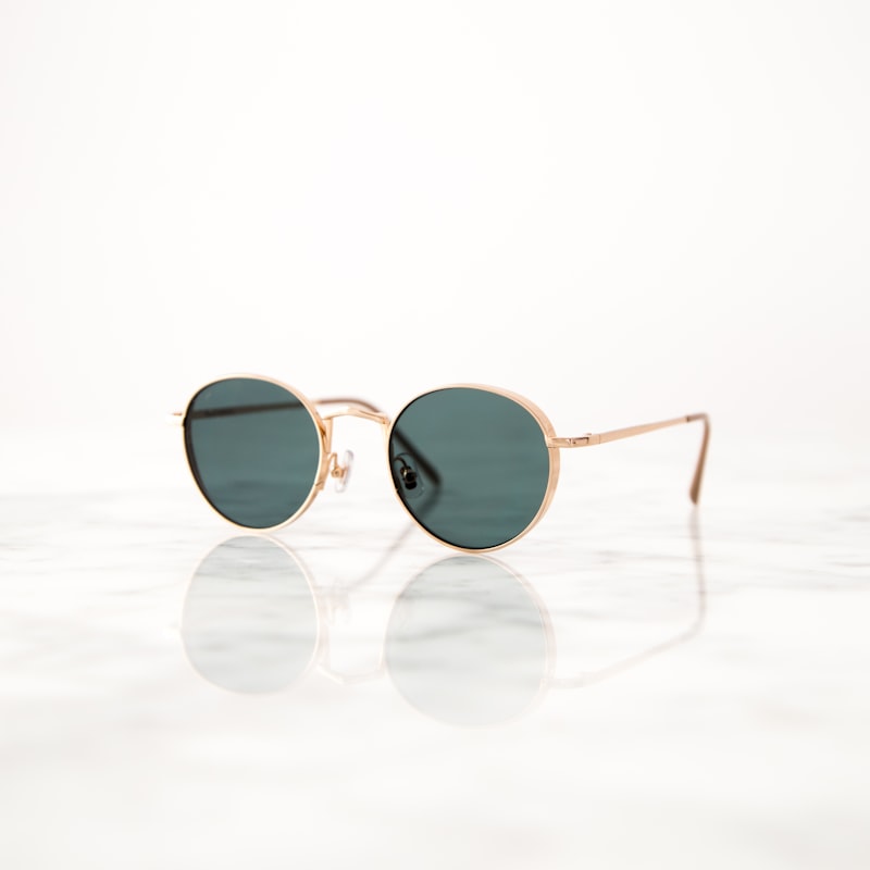 Lunet Mercer round sunglasses in gold wire with dark green lenses on a marble surface