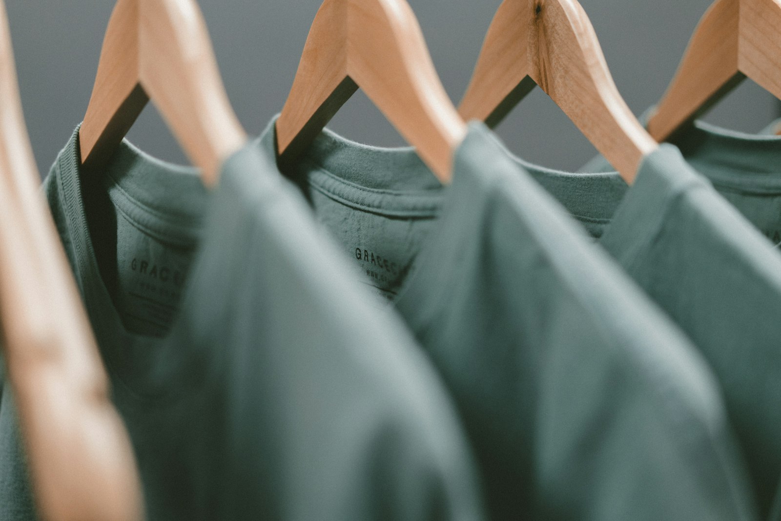 Row of dark green cotton t-shirts hanging on wooden hangers on a rail