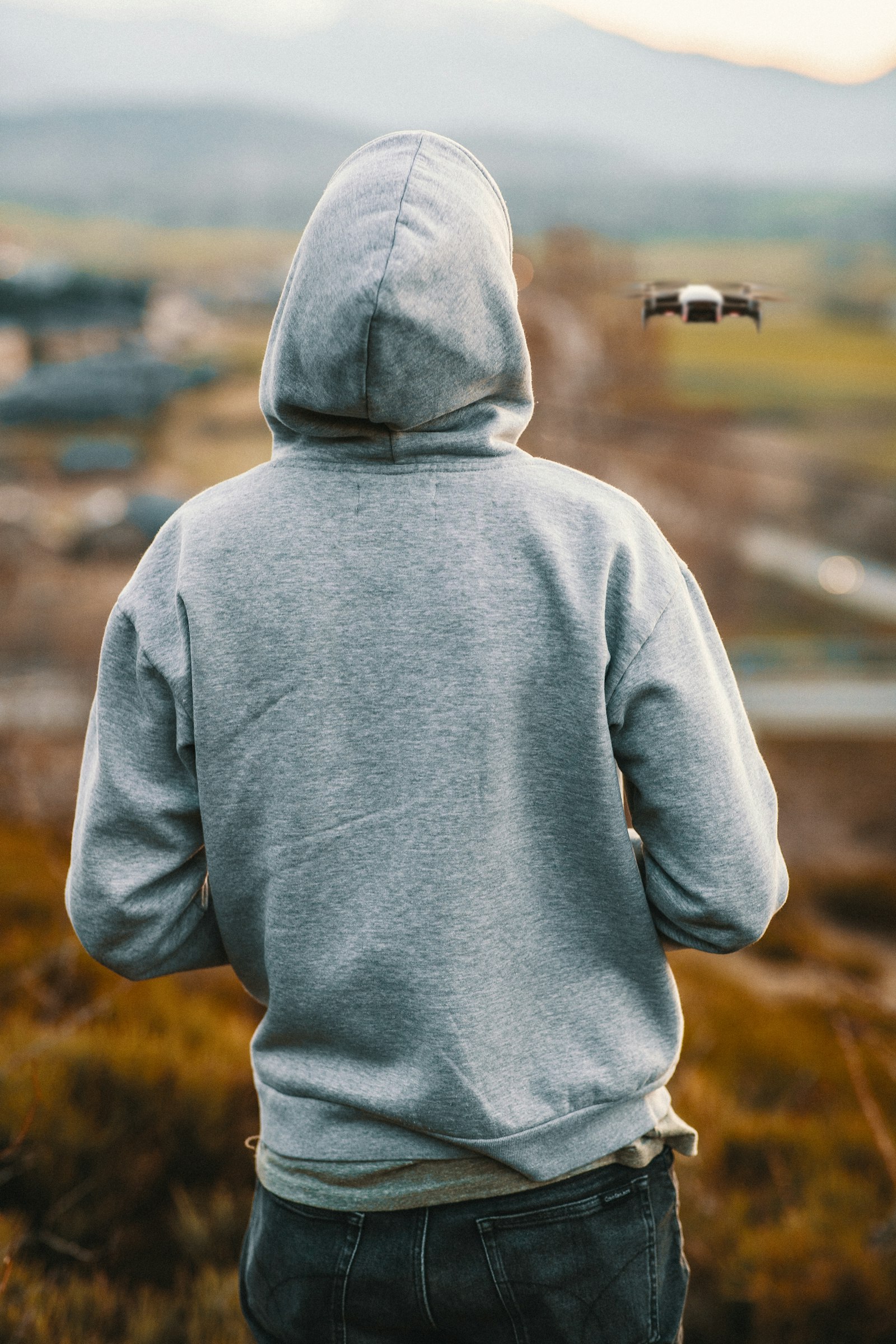Back view of a plain grey pullover hoodie worn outdoors