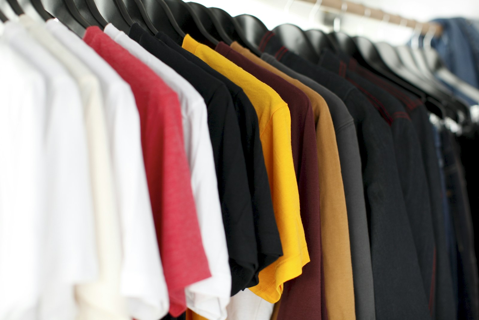 Row of plain cotton tees in white, red, black and ochre hanging on a rail