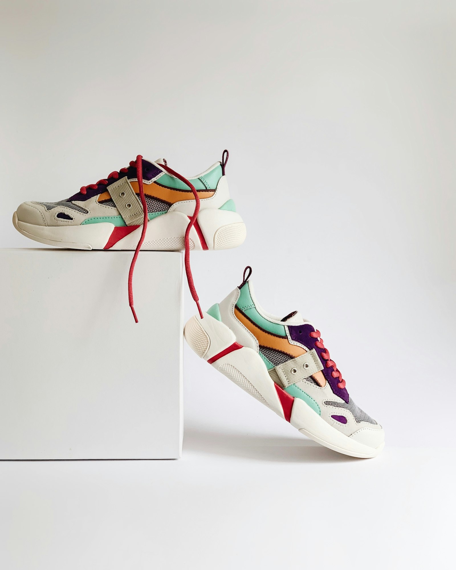 Pair of panelled low-top sneakers balanced on a white studio plinth