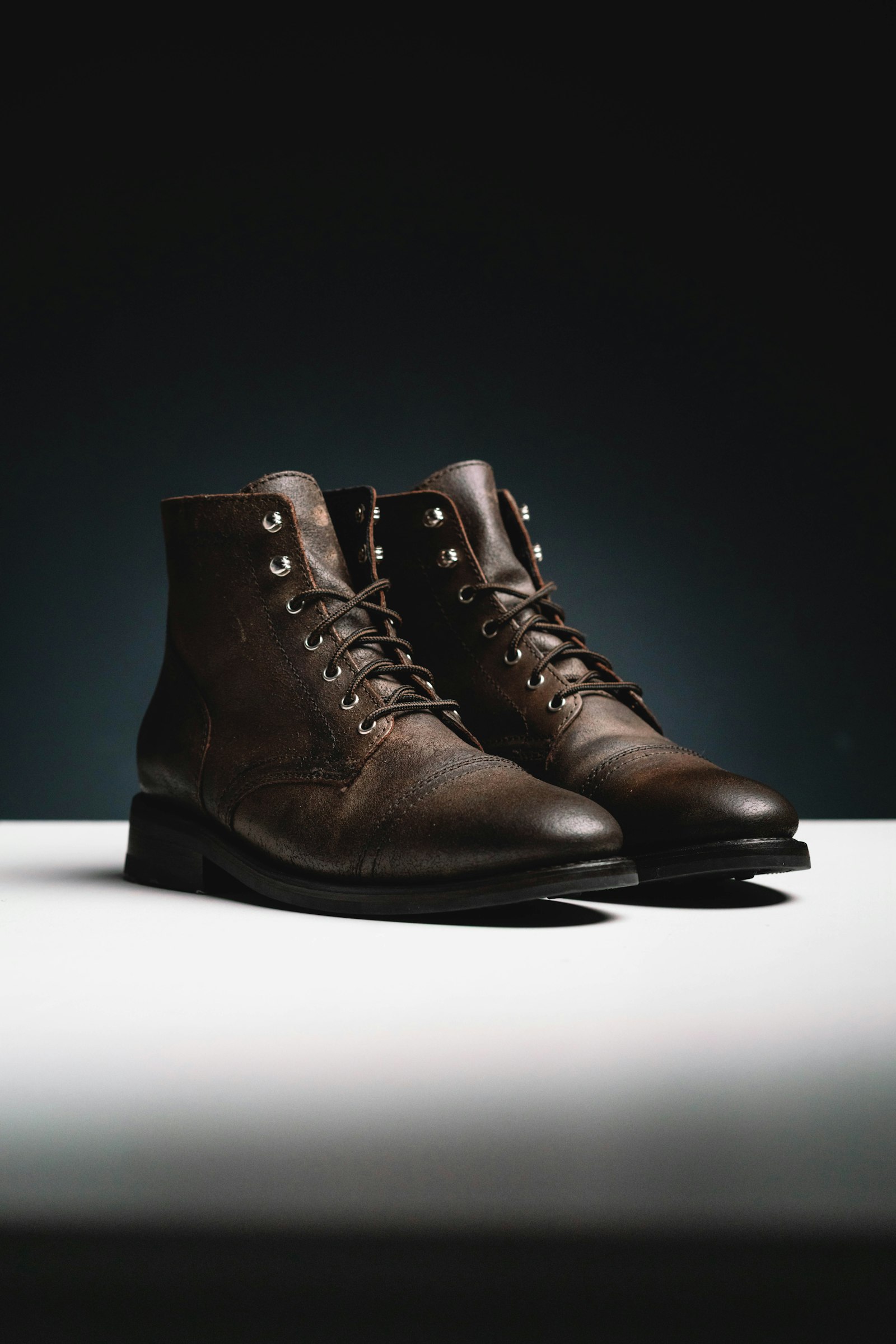 Pair of brown waxed-leather lace-up boots on a white plinth against a dark background