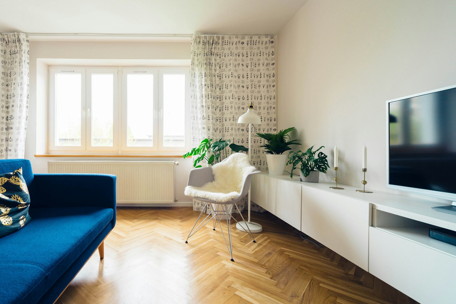 Scandinavian living room with a blue daybed sofa, white shell chair and a low white sideboard on herringbone parquet