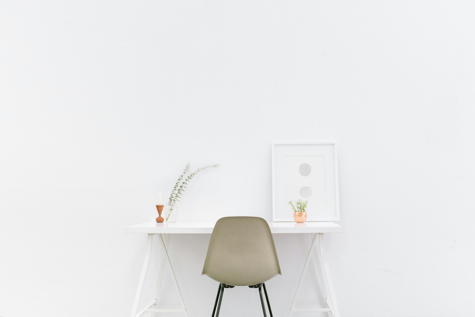 Minimal white trestle desk against a white wall with a moulded shell chair and a single vase