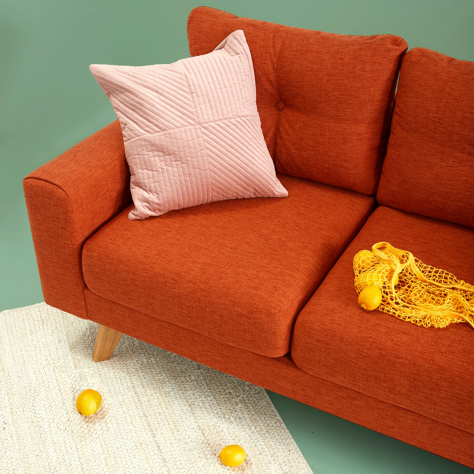 Rust-orange woven fabric two-seater sofa with tapered oak legs and a blush quilted cushion