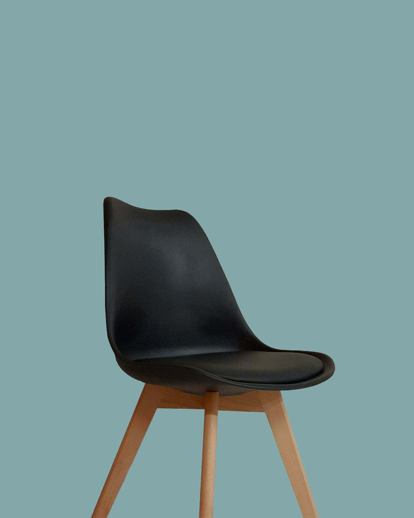 Black moulded shell dining chair on tapered natural beech legs against a muted teal backdrop
