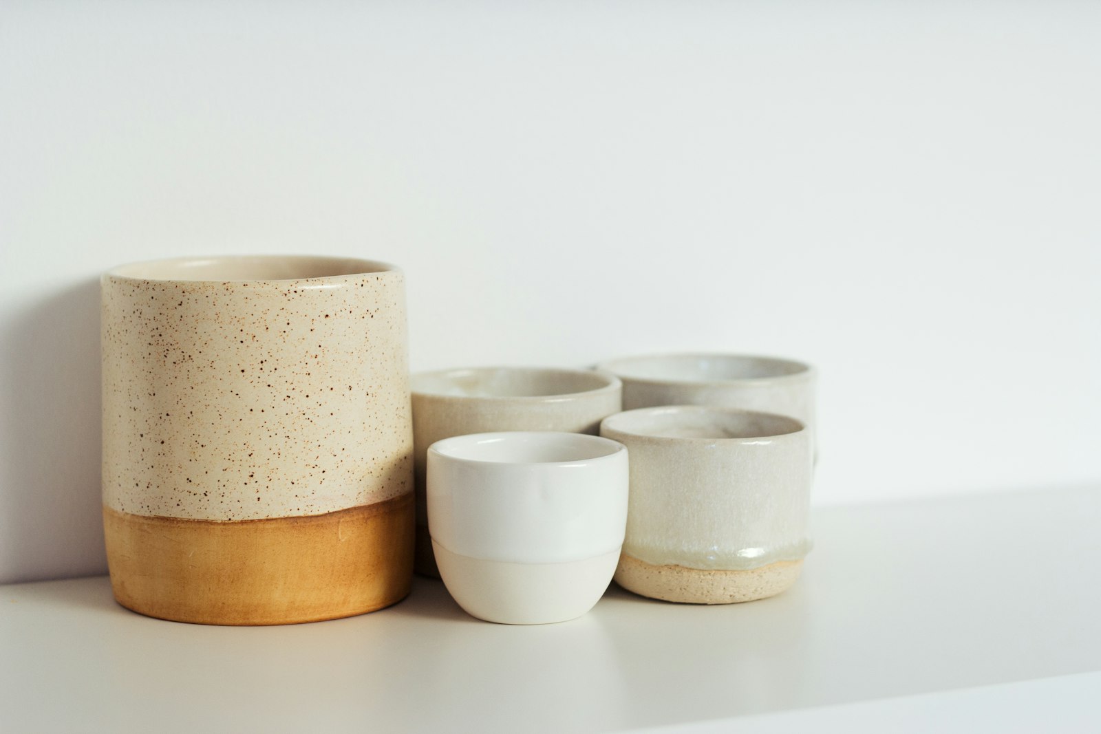 Four unglazed and half-glazed stoneware vessels in oat and clay tones on a white surface