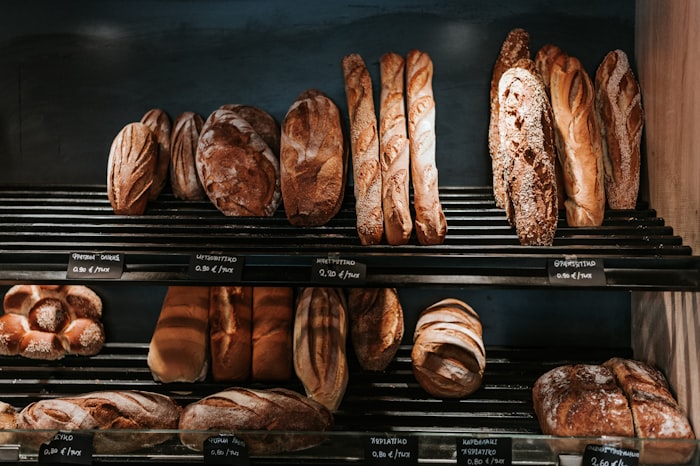 Sourdough loaves and baguettes cooling on a bakery rack above chalked price rails