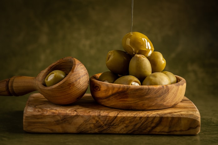 Green olives in an olive-wood bowl being dressed with oil