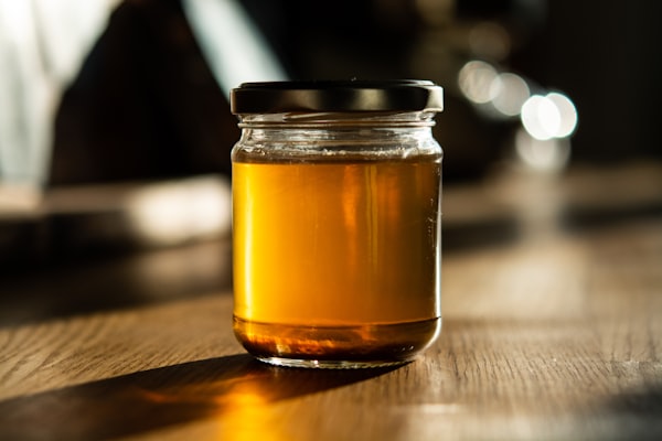 An unlabelled glass jar of raw honey glowing in afternoon light