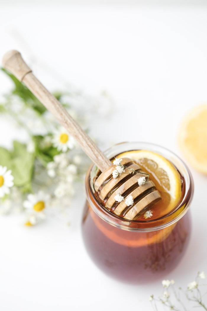A jar of honey with a dipper, chamomile flowers and a lemon half