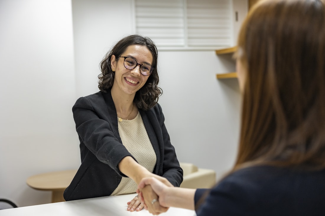A hiring manager shaking hands with a candidate across a table at the end of an interview