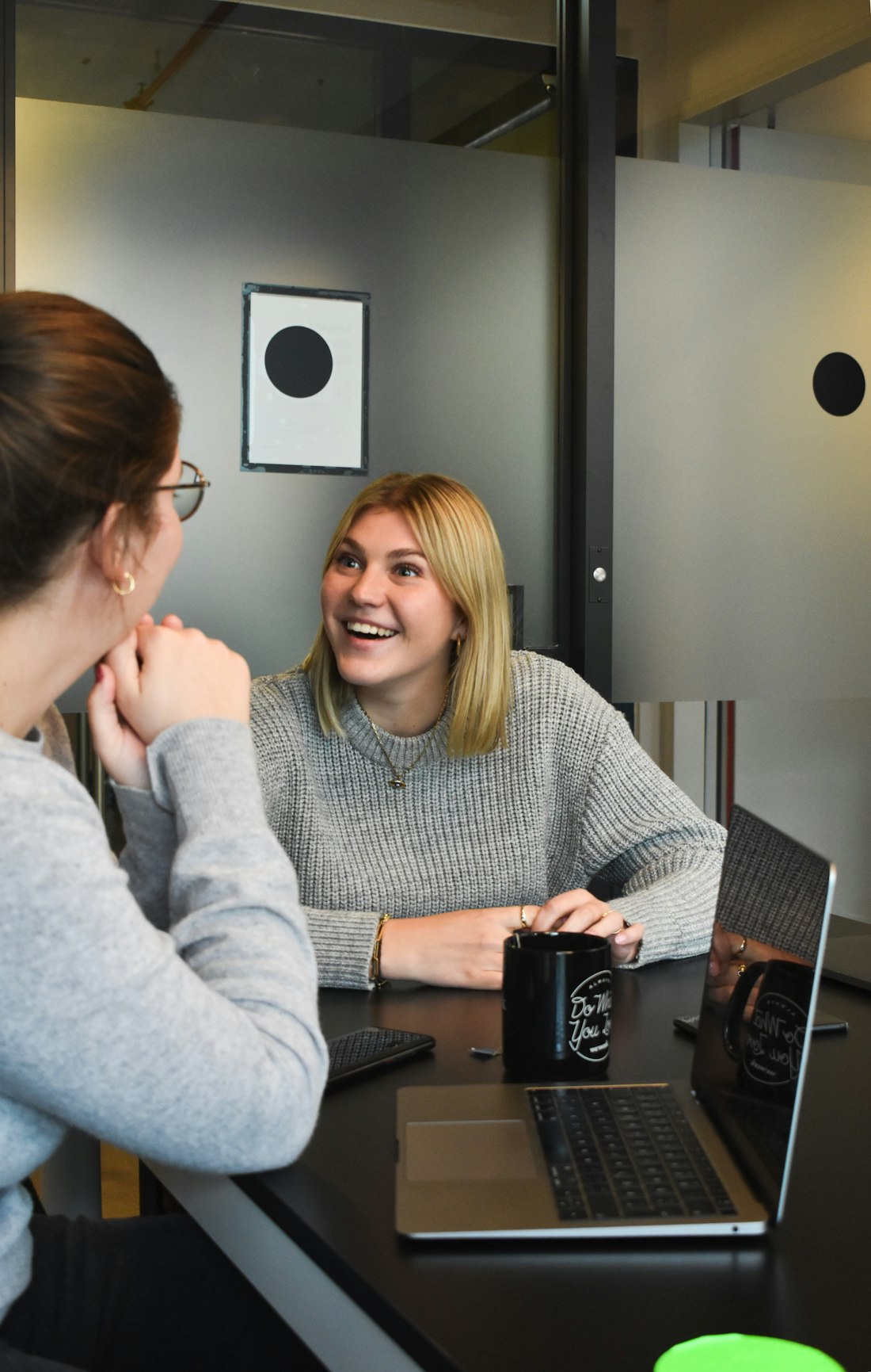 Two colleagues laughing together during a one-to-one conversation at a table