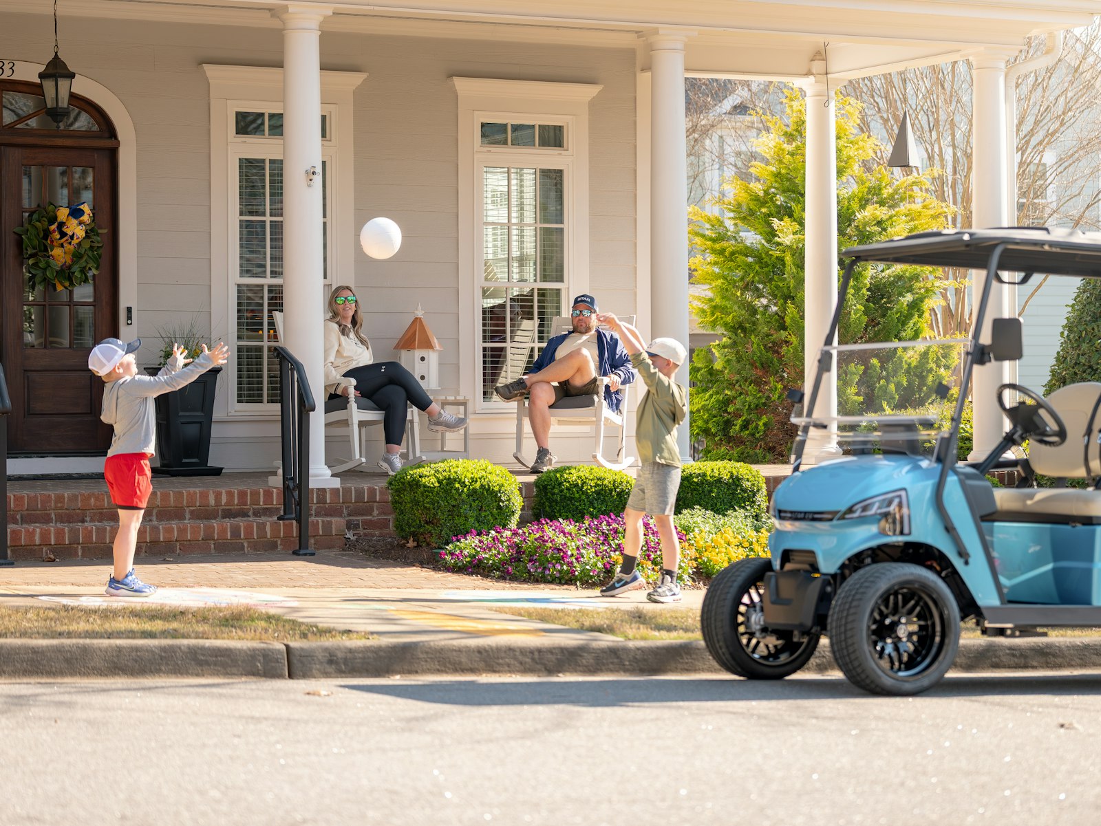 A family on their front porch on a sunny afternoon, kids playing in the yard