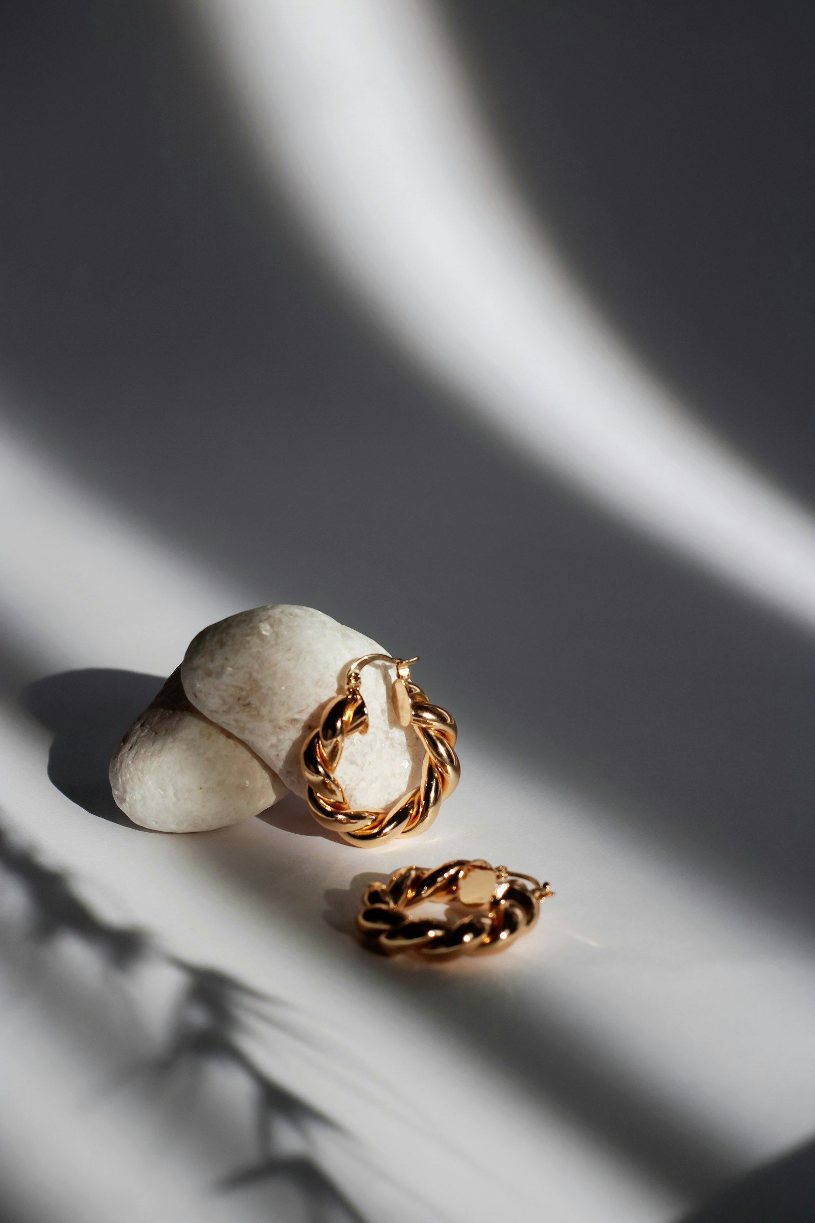 The Torsade twisted gold hoop earrings resting on a pale river stone