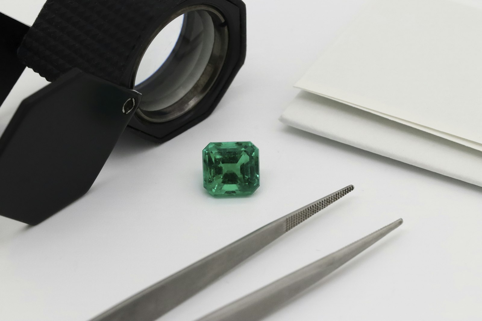 A loose emerald under a jeweller's loupe beside steel tweezers on the Auverre grading bench