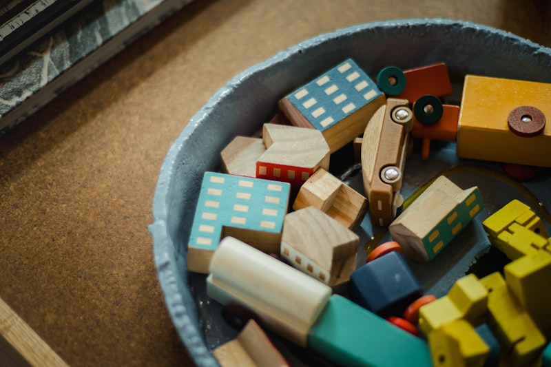 A tray of small wooden town pieces — painted houses, a fire engine and vehicles in soft blues and yellows.