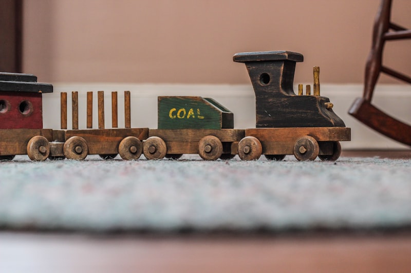 A hand-finished wooden freight train with a dark engine, coal wagon and open carriages on a rug.