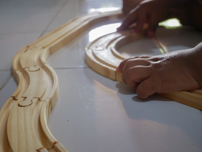 A child's hands laying out curved beech track pieces on the floor to complete a loop.