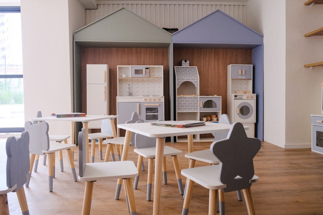 A child's playroom with wooden play kitchens, small tables and star-backed chairs in soft grey and beech.