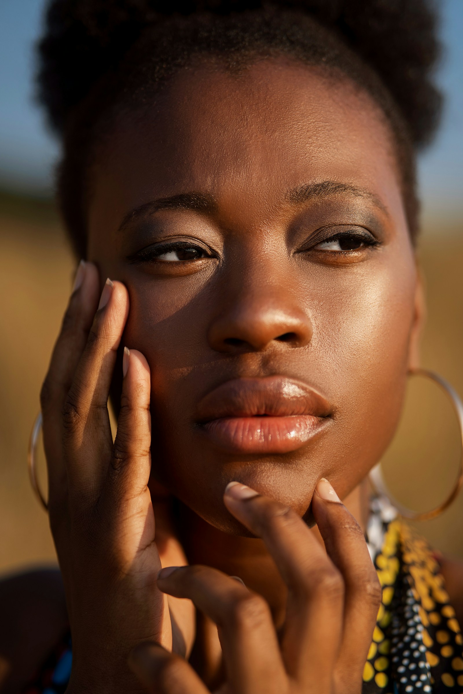 A woman resting both hands against her cheek and chin in late afternoon light, skin unretouched.