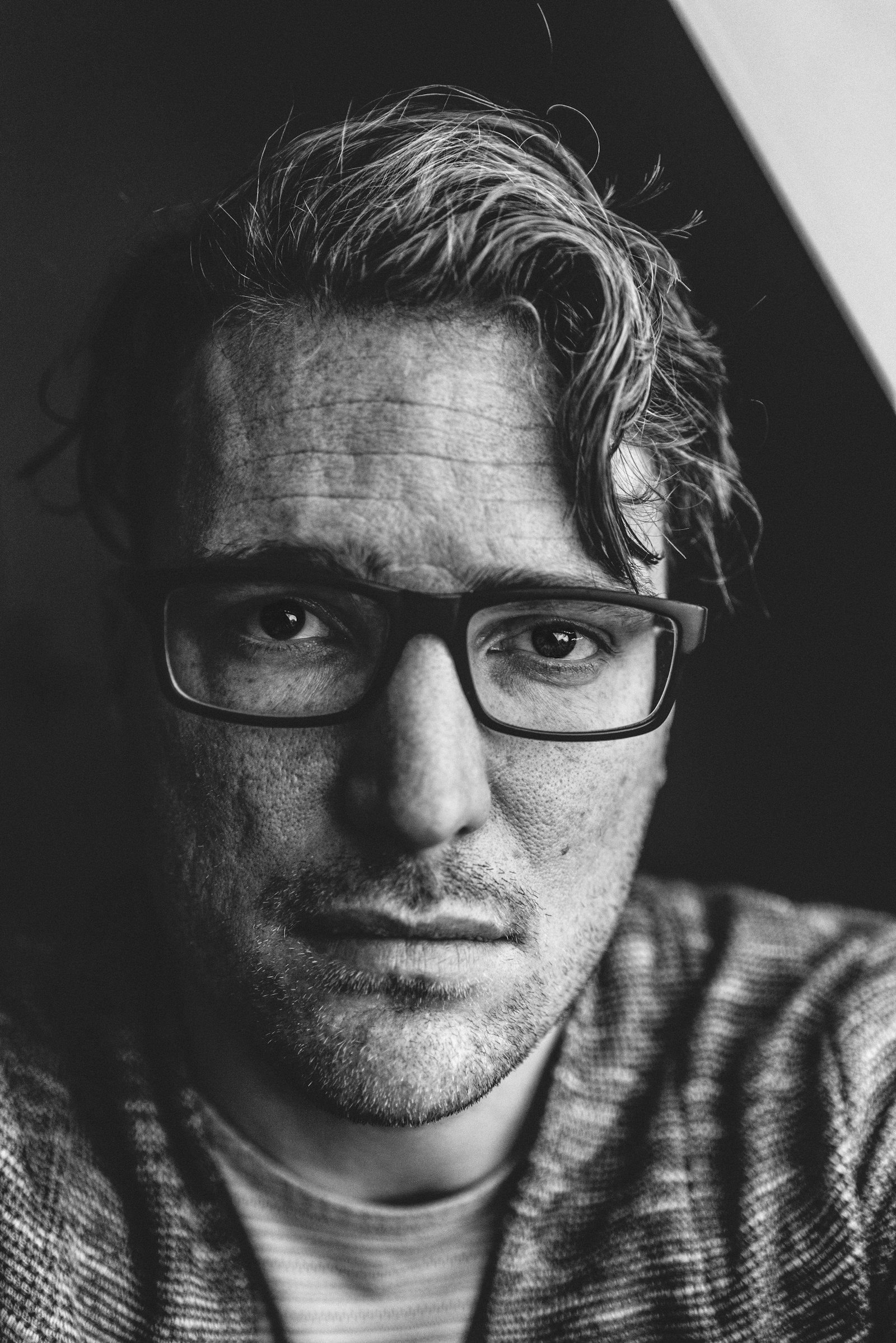 Black and white portrait of a man in rectangular dark-framed spectacles and a knitted cardigan