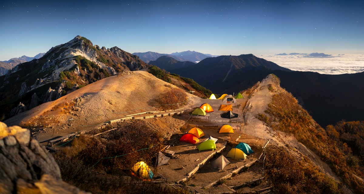 Tents pitched on a high alpine ridge camp at dusk above a cloud inversion