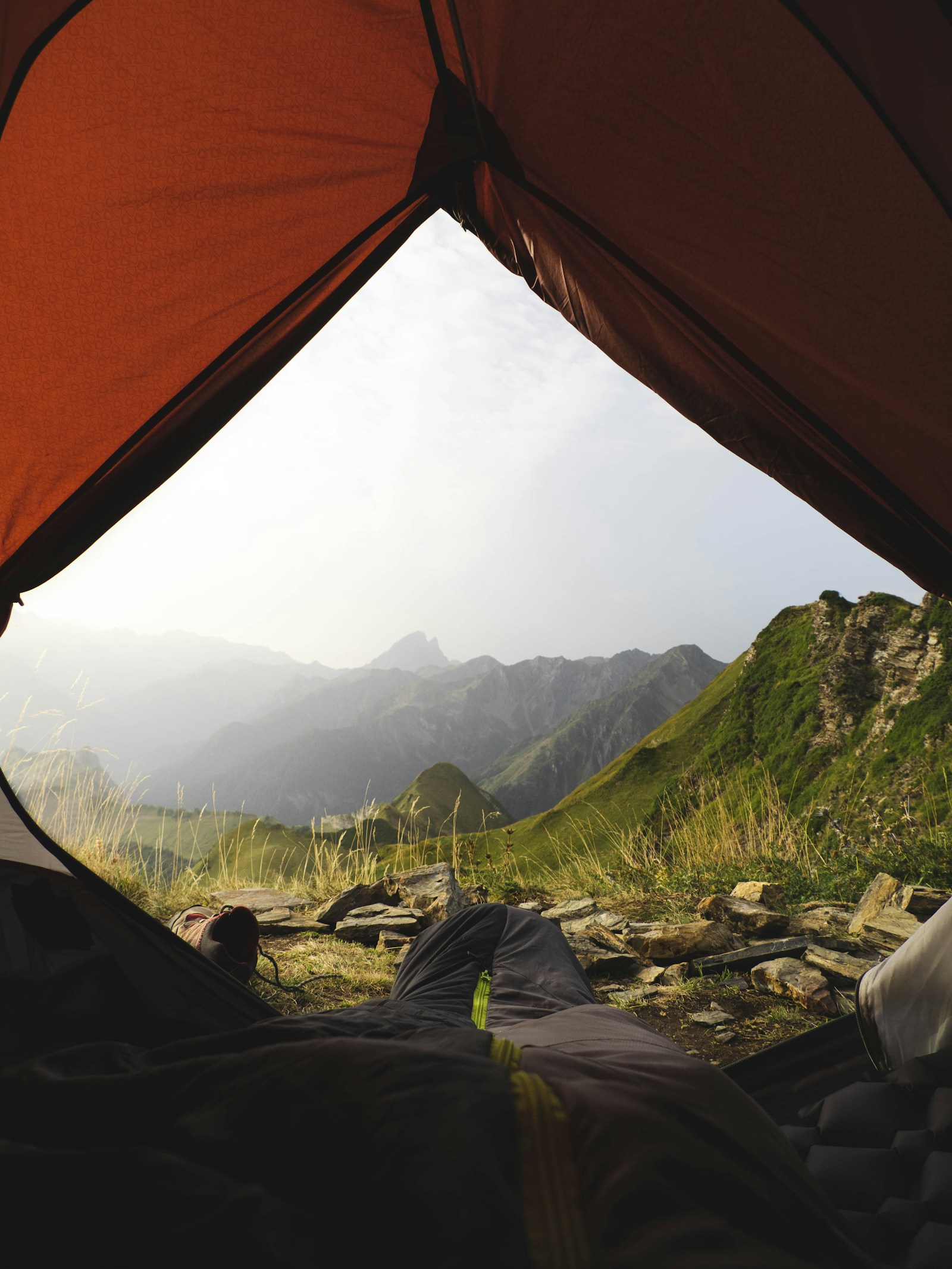 Dawn from inside a tent doorway, looking out at a green alpine ridge