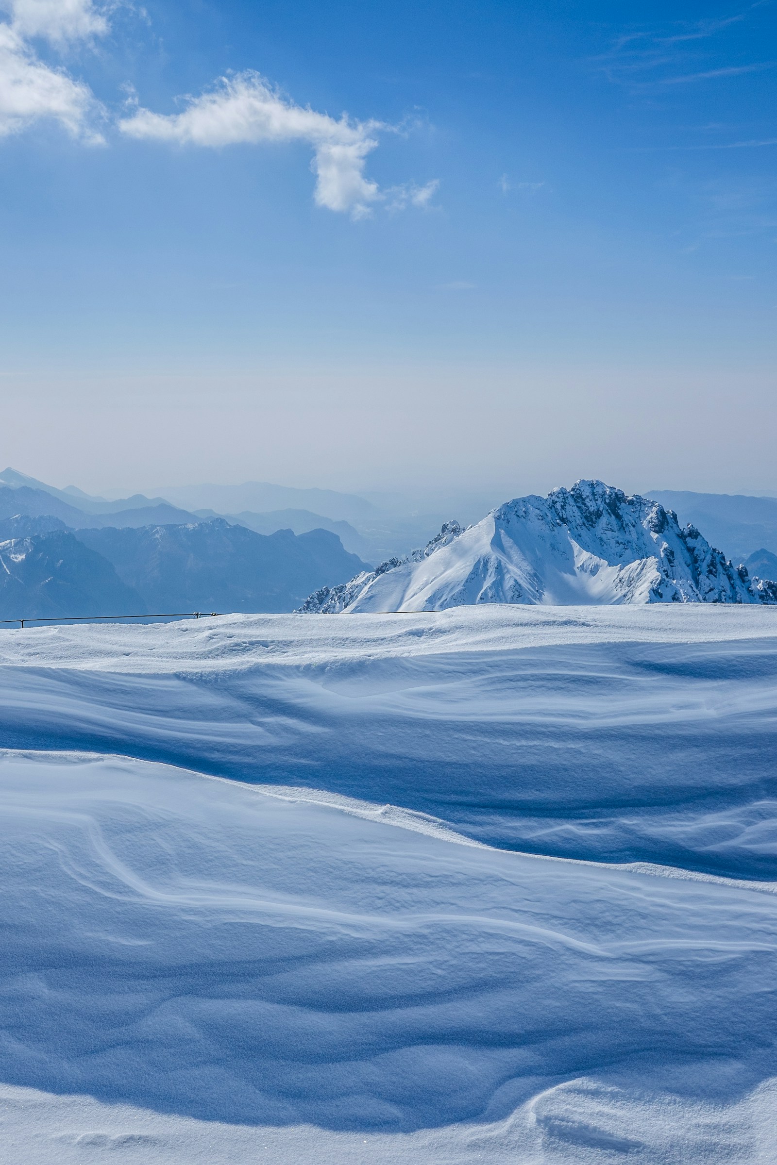 Wind-sculpted snowfield running to a rocky summit ridge under a clear winter sky