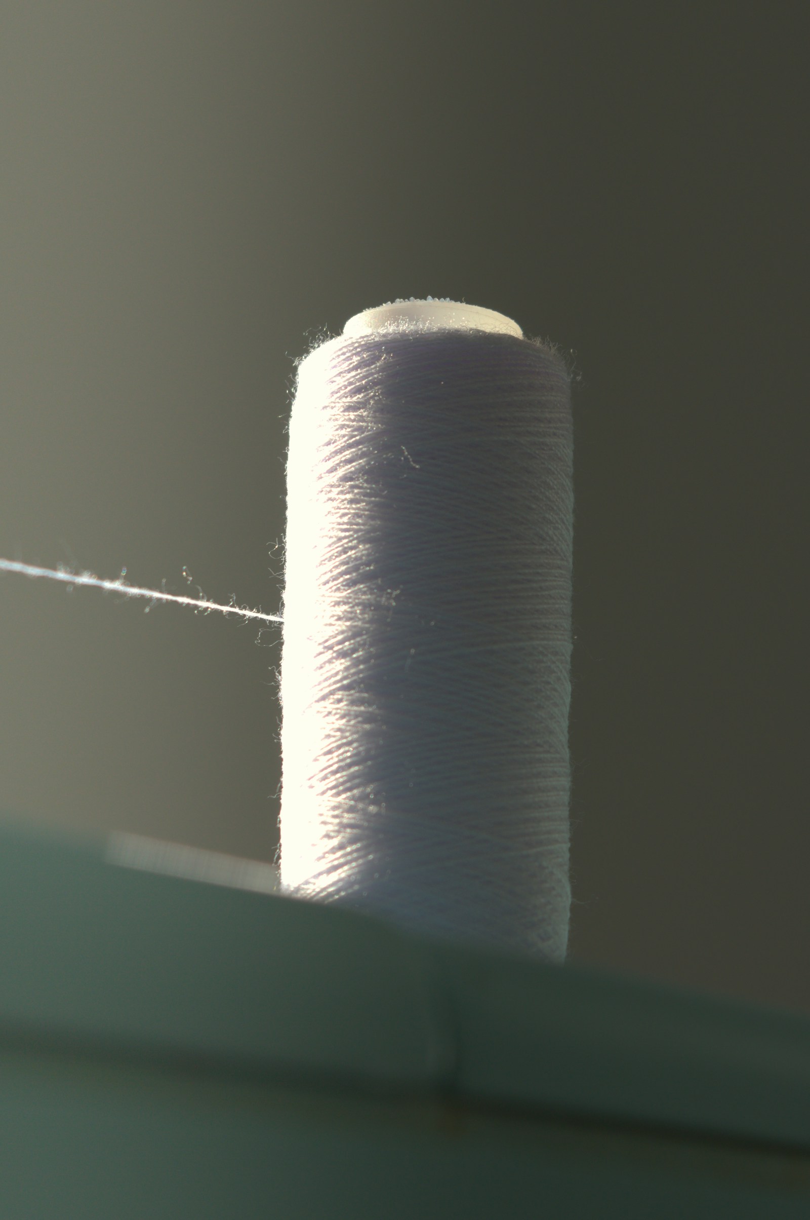 Backlit spool of white bonded thread with a single strand running off it