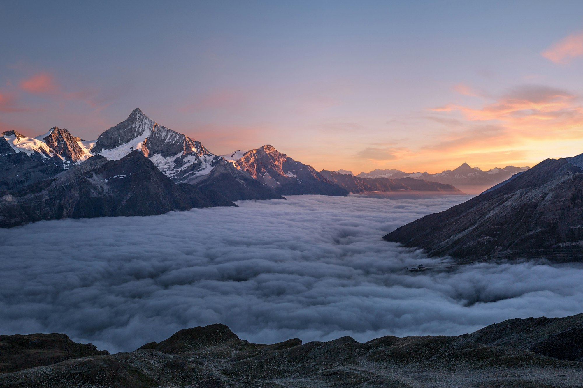 Snow-capped peaks at first light above a valley filled with low cloud