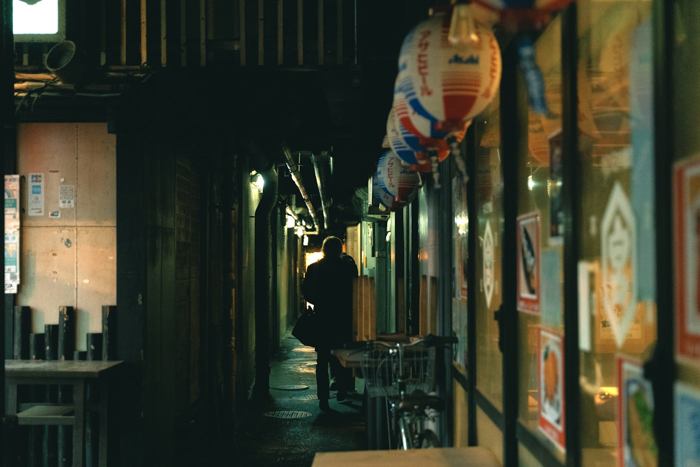Lone figure walking a narrow Tokyo back-alley at night under warm sodium lamps