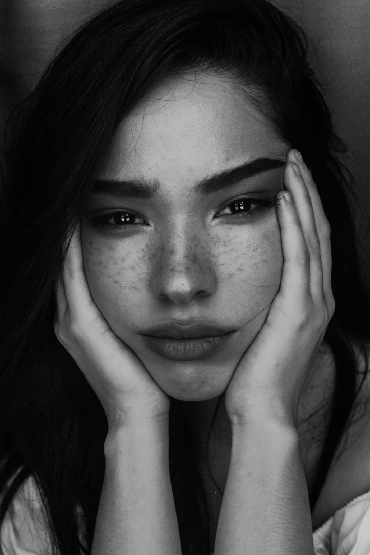 Monochrome portrait of a woman in low tonal light, hands framing a face half sunk in shadow