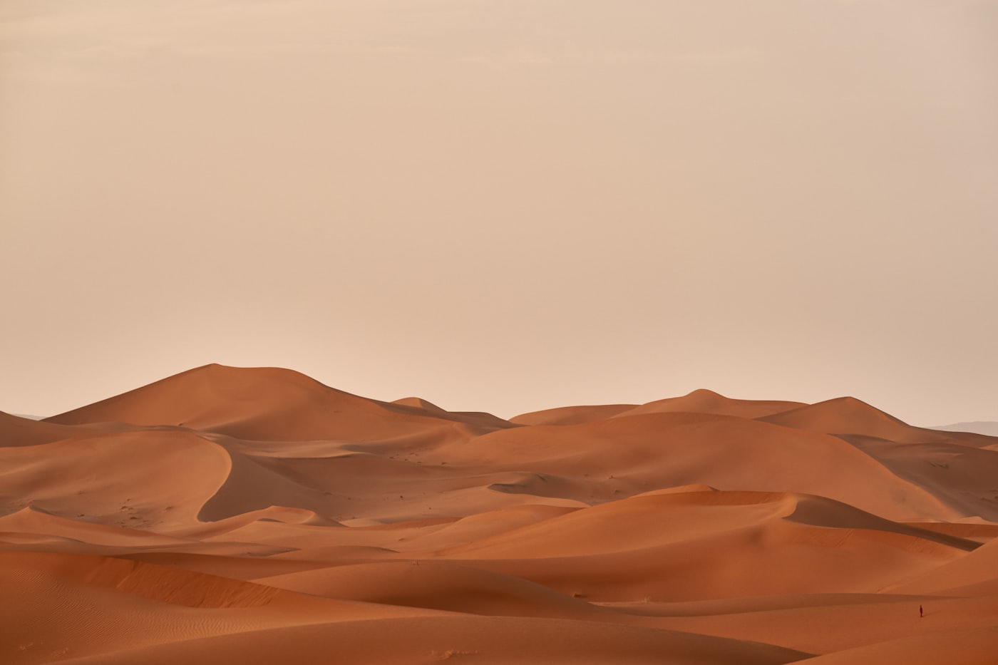 Red desert dunes receding into haze, wind-carved shadow along the crest lines